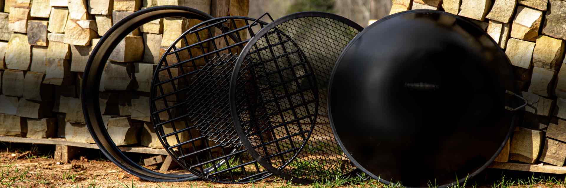 Fire ring, fire grate, BBQ grate and a fire pit lid or cover propped against stacks of wood